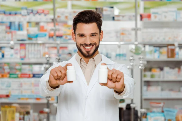 Droga sorridente olhando para a câmera e segurando frascos com pílulas — Fotografia de Stock