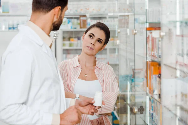 Customer with crossed arms looking at pharmacist with pills by drugstore showcase — Stock Photo