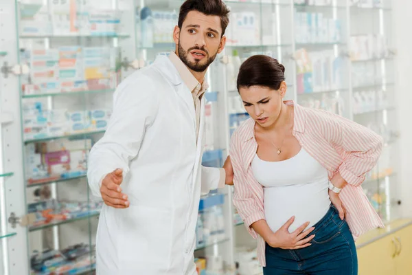 Farmacêutico ajudando a mulher grávida com dor na farmácia — Fotografia de Stock