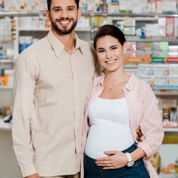 Sourire femme enceinte à côté du mari avec vitrine de pharmacie à l'arrière-plan — Photo de stock