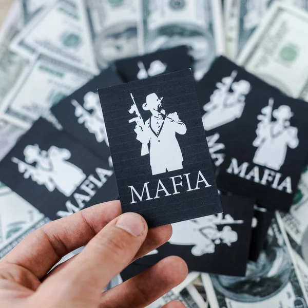 KYIV, UKRAINE - NOVEMBER 22, 2019: cropped view of man holding playing card with mafia letters near cash — Stock Photo