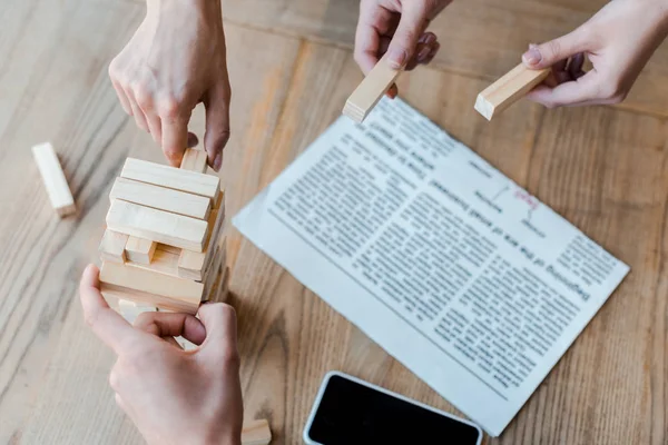 KYIV, UCRAINA - 22 NOVEMBRE 2019: vista ritagliata delle donne che giocano ai blocchi di legno torre di gioco vicino allo smartphone con schermo bianco — Foto stock