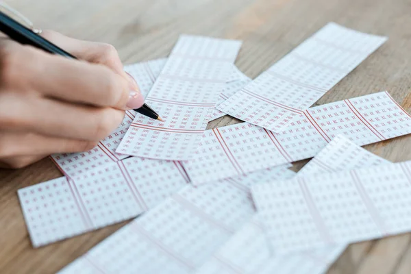 Vista cortada de mulher segurando caneta perto de bilhetes de loteria na mesa — Fotografia de Stock