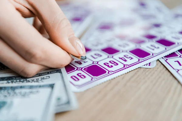 Vista recortada de la mujer sosteniendo moneda y rascando billete de lotería en la mesa - foto de stock