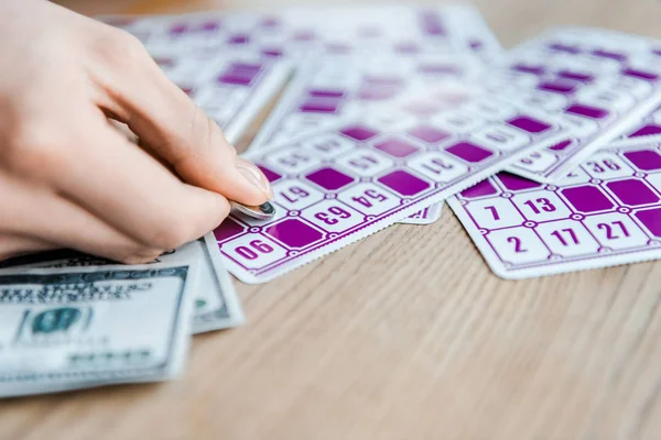 Vista recortada de la mujer sosteniendo moneda y rascando billete de lotería cerca de efectivo - foto de stock