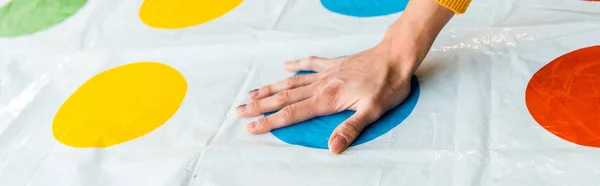 KYIV, UCRANIA - 22 de noviembre de 2019: plano panorámico de la mujer poniendo la mano en el círculo azul mientras juega al twister game - foto de stock