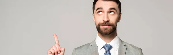 Tiro panorâmico de homem de negócios sorridente olhando para longe ao mostrar gesto ideia isolado em cinza — Fotografia de Stock