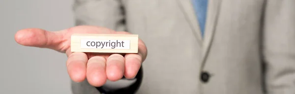 Partial view of businessman showing wooden block with word copyright isolated on grey, panoramic shot — Stock Photo