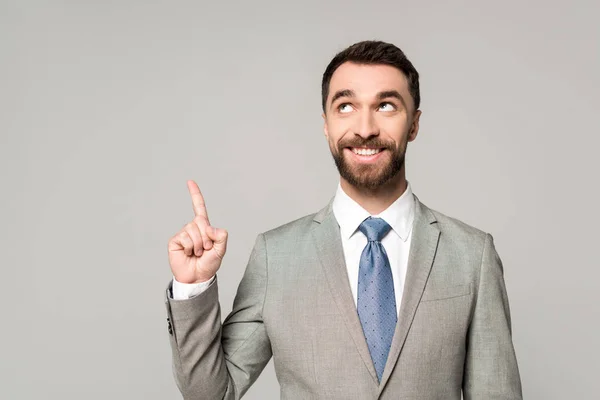 Alegre hombre de negocios mirando hacia otro lado mientras muestra gesto de idea aislado en gris - foto de stock