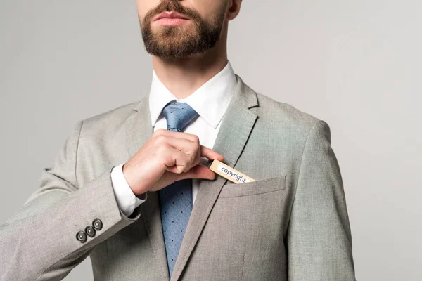 Vista parziale di uomo d'affari mettendo blocco di legno con diritto d'autore parola in tasca isolato su grigio — Foto stock