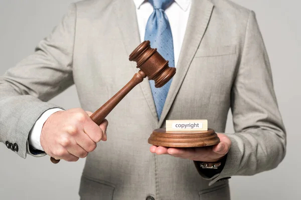 Cropped view of judge holding gavel near wooden block with copyright inscription isolated on grey — Stock Photo