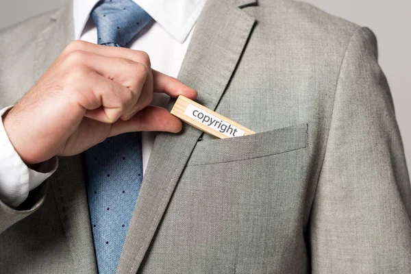 Abgeschnittene Ansicht eines Geschäftsmannes, der Holzblock mit Worturheberrecht in die Tasche steckt, isoliert auf grau — Stockfoto