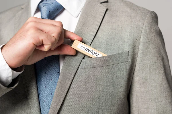 Cropped view of businessman putting wooden block with word copyright in pocket isolated on grey — Stock Photo