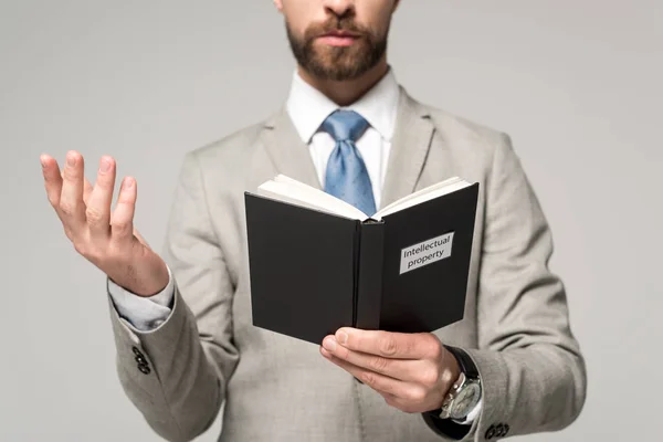 Vista recortada del hombre de negocios leyendo libro con título de propiedad intelectual aislado en gris - foto de stock