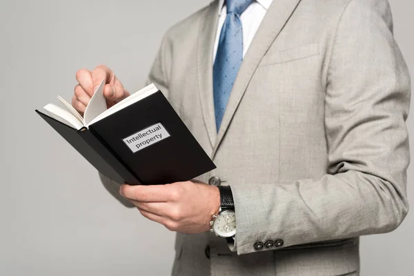 Abgeschnittene Ansicht eines Geschäftsmannes, der Buch mit geistigem Eigentum liest, isoliert auf grau — Stockfoto