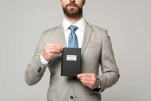 Vista recortada del empresario con libro jurídico con título de propiedad intelectual aislado en gris - foto de stock