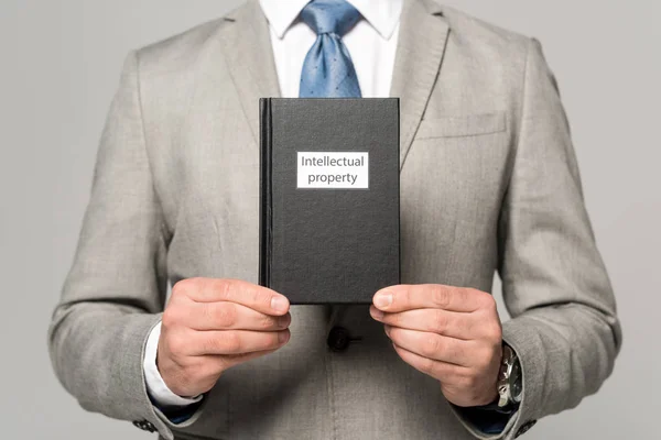 Teilansicht des Geschäftsmannes mit juristischem Buch mit geistigem Eigentum isoliert auf grau — Stockfoto
