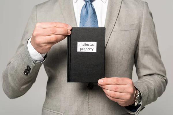 Visión parcial del empresario con libro jurídico con título de propiedad intelectual aislado sobre gris - foto de stock