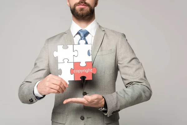 Abgeschnittene Ansicht von Geschäftsmann hält Puzzle mit Urheberrechtsbeschriftung isoliert auf grau — Stockfoto