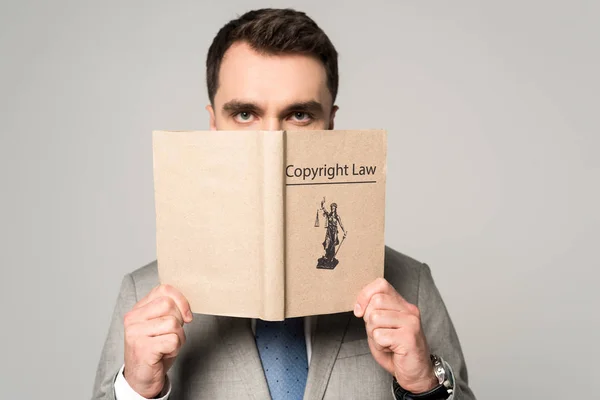 Serious lawyer looking at camera while holding book with copyright law title isolated on grey — Stock Photo