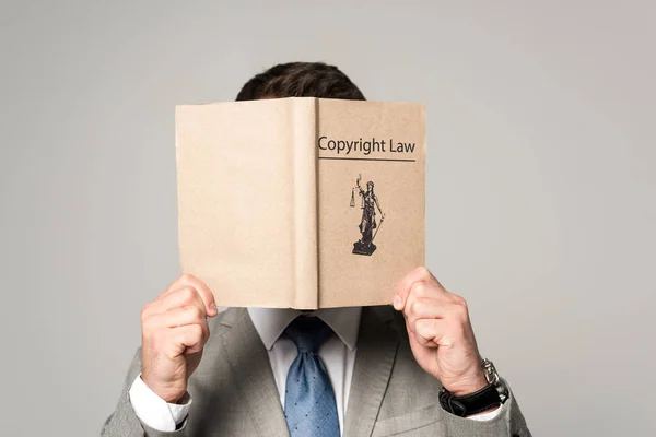 Lawyer obscuring face with copyright law book isolated on grey — Stock Photo