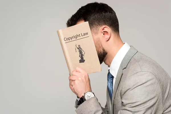Side view of lawyer obscuring face with copyright law book isolated on grey — Stock Photo