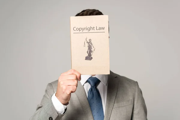 Вид спереди адвоката, скрывающего лицо книгой по авторскому праву, изолированной на сером фоне — стоковое фото