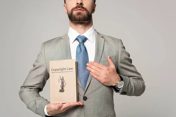 Частичный взгляд юриста, держащего руку на сердце и книгу с авторским правом название изолированы на серый — стоковое фото