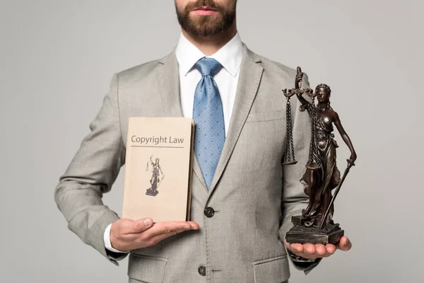 Vista cortada de advogado segurando themis estátua e livro com direito autoral título isolado em cinza — Fotografia de Stock