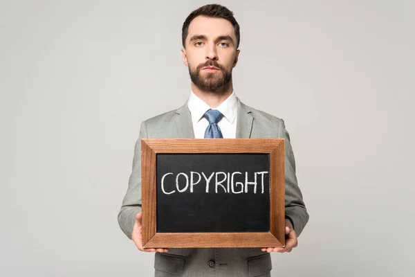 Fiducioso uomo d'affari che tiene la lavagna con scritte di copyright isolate su grigio — Foto stock