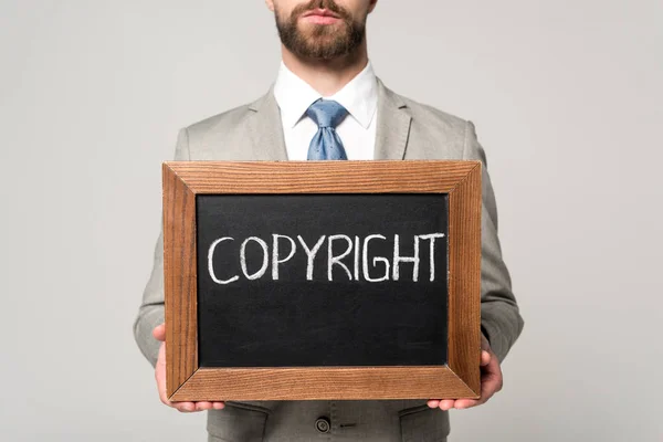 Vista recortada del hombre de negocios sosteniendo pizarra con letras de copyright aisladas en gris - foto de stock