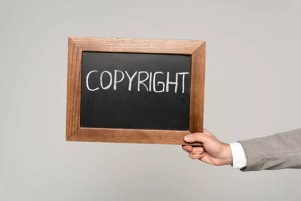 Cropped view of businessman holding chalkboard with copyright inscription isolated on grey — Stock Photo