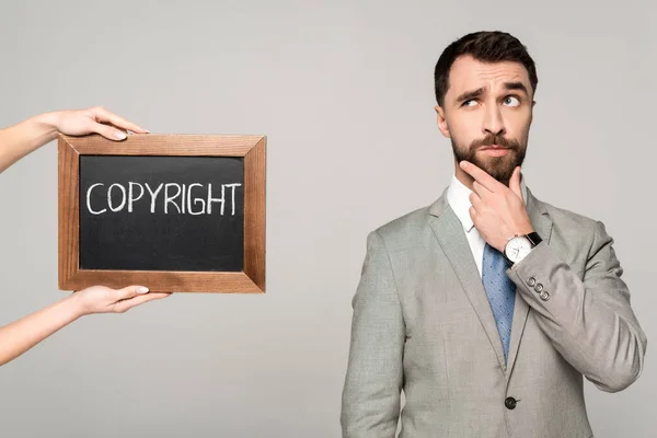 Partial view of woman holding chalkboard with copyright inscription near thoughtful businessman isolated on grey — Stock Photo