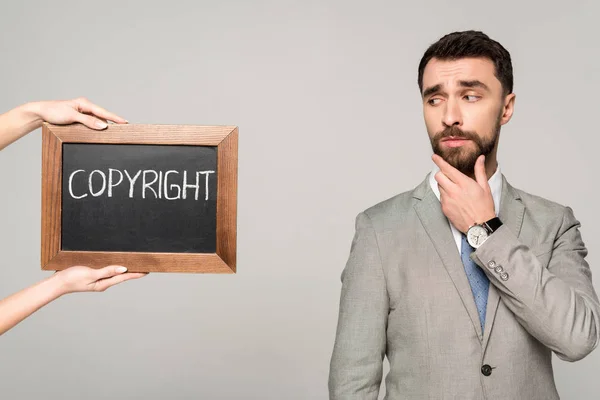 Partial view of woman holding chalkboard with copyright inscription near skeptical businessman isolated on grey — Stock Photo