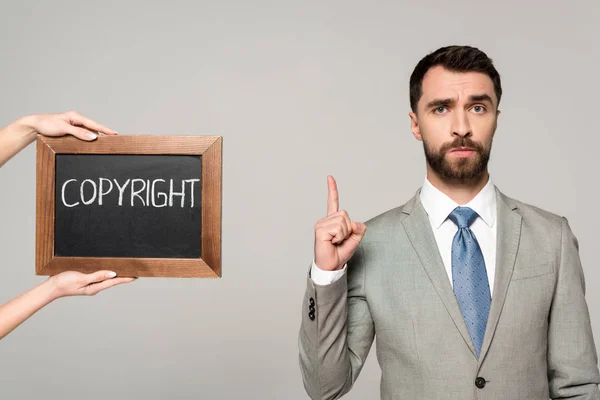 Teilansicht einer Frau mit Kreidetafel mit Urheberrechtsbeschriftung in der Nähe eines Geschäftsmannes, die Ideenschild isoliert auf grau zeigt — Stockfoto