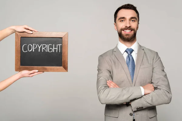 Partial view of woman holding chalkboard with copyright inscription near businessman smiling at camera isolated on grey — Stock Photo