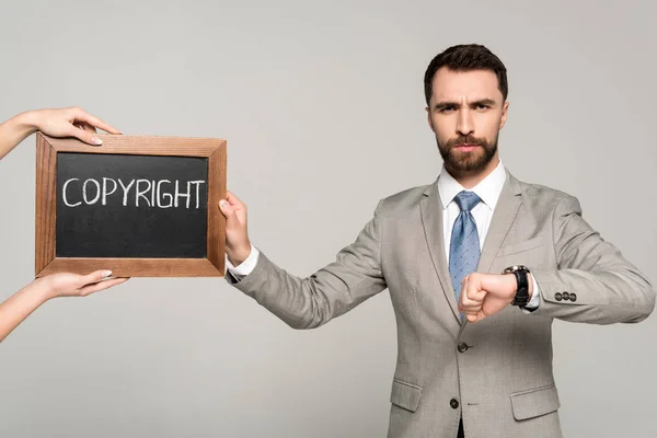 Vista ritagliata della donna che tiene la lavagna con iscrizione sul copyright vicino all'uomo d'affari guardando la fotocamera isolata sul grigio — Foto stock