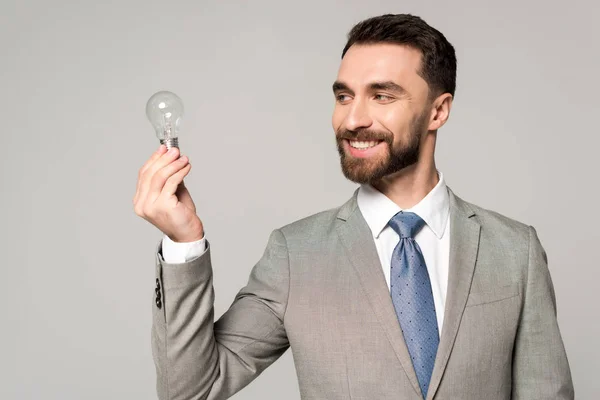 Uomo d'affari sorridente che tiene la lampadina isolata sul grigio — Foto stock