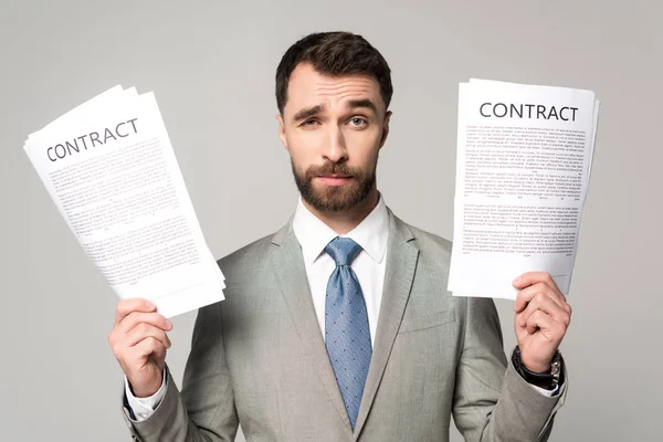 Skeptical businessman holding contracts and looking at camera isolated on grey — Stock Photo