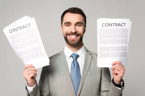 Happy businessman holding contracts and looking at camera isolated on grey — Stock Photo