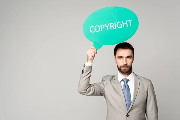 Seriöser Geschäftsmann hält Gedankenblase mit Urheberrechtsinschrift isoliert auf grau — Stockfoto