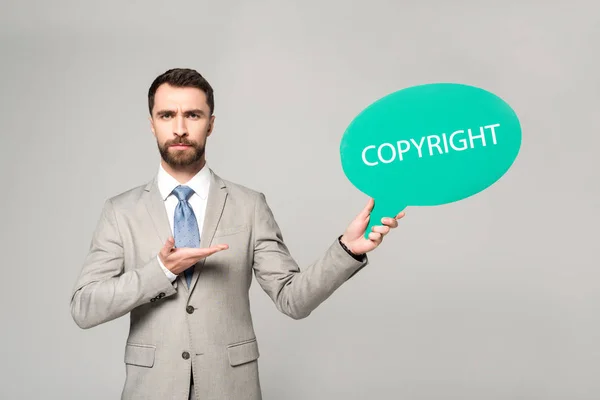 Hombre de negocios confiado apuntando con la mano a la burbuja del pensamiento con la inscripción del copyright aislada en gris - foto de stock