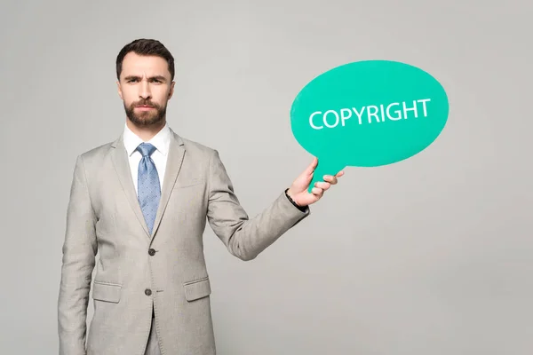 Hombre de negocios confiado sosteniendo la burbuja del pensamiento con la inscripción del copyright aislada en gris - foto de stock