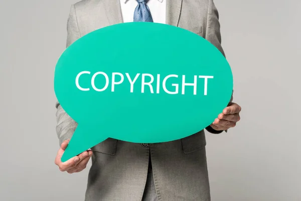 Vista ritagliata dell'uomo d'affari che tiene bolla di pensiero con iscrizione di copyright isolata su grigio — Foto stock