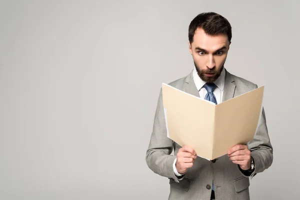 Shocked businessman looking at documents in paper folder isolated on grey — Stock Photo