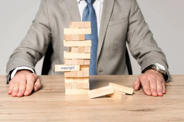 Partial view of businessman near blocks wood tower game with copyright inscription isolated on grey — Stock Photo