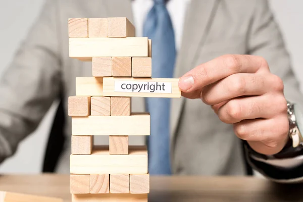 Vista parcial de hombre de negocios cerca de bloques torre de madera juego con inscripción de derechos de autor aislado en gris — Stock Photo