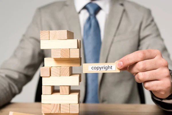 Partial view of businessman holding wooden block with copyright inscription isolated on grey — Stock Photo