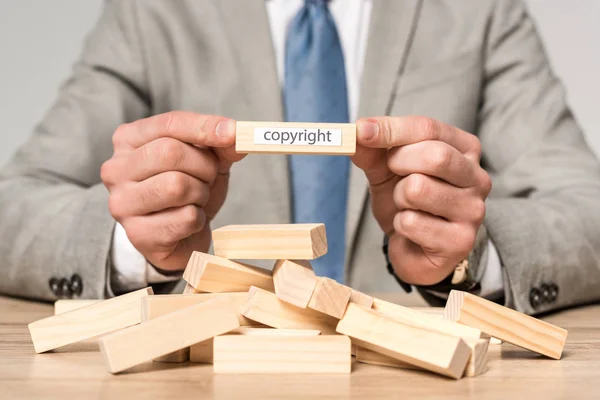 Vista parcial del empresario sosteniendo un bloque de madera con inscripción de derechos de autor aislado en gris - foto de stock