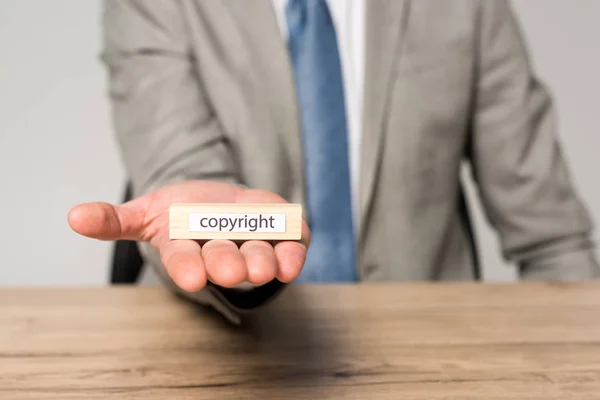 Vista recortada del hombre de negocios sosteniendo un bloque de madera con inscripción de derechos de autor aislado en gris — Stock Photo